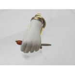 A hand carved white stone pendant in the form of a clenched fist holding a dagger with a red handle.