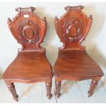 A fine pair of Victorian mahogany hall chairs with detailed carved panels.