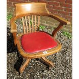 A 20th Century oak framed captains swivel desk chair with a red leather upholstered seat with