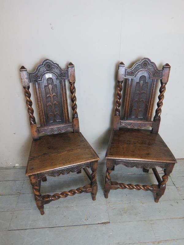 A pair of 17th Century oak hall chairs with carved motifs and spiral twist uprights and lower front