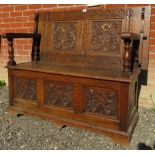 A 20th Century oak monk's bench with a carved back over a lift up storage compartment and three