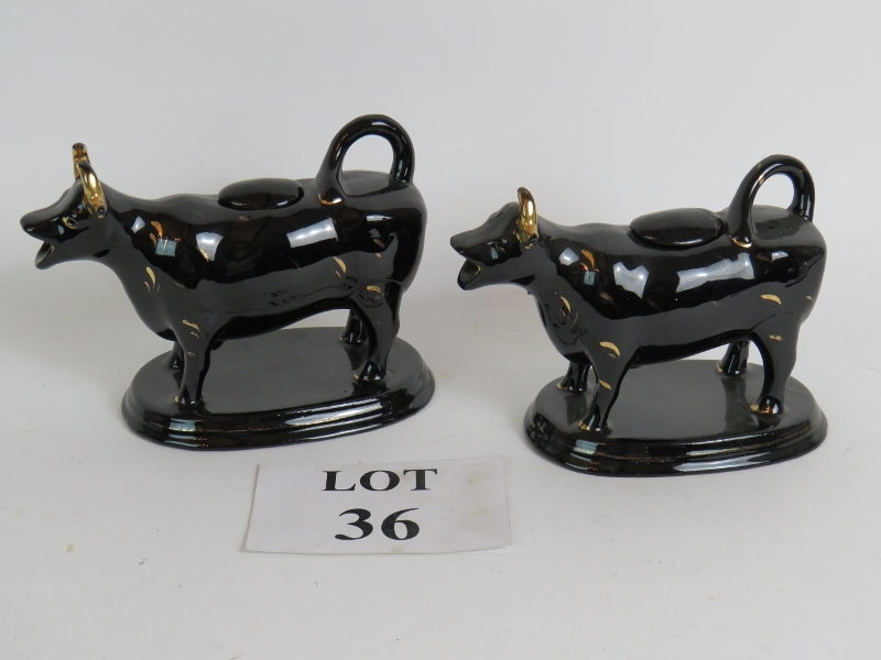 A pair of antique black glazed cow cream