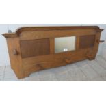 A British Arts & Crafts oak coat rack, with shaped cornice above central mirror and 5 pegs.
