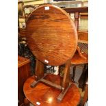 AN OAK FINISHED CIRCULAR TILT TOP TABLE on shaped plank uprights