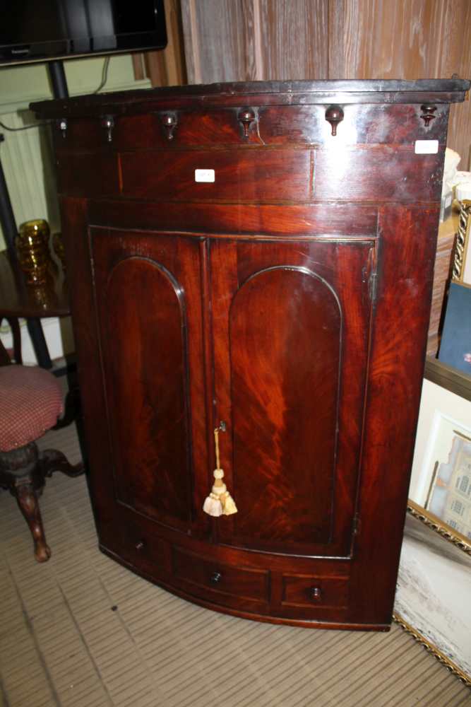 A 19TH CENTURY LARGE BOW FRONT HANGING CORNER CUPBOARD with twin plain panel doors, revealing