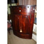 A 19TH CENTURY LARGE BOW FRONT HANGING CORNER CUPBOARD with twin plain panel doors, revealing