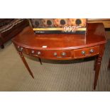 A REPRODUCTION BOW FRONTED MAHOGANY FINISHED SIDE TABLE having three inline drawers, supported on