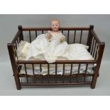 AN ARMAND MARSEILLE BISQUE HEADED DOLL on composition body, in early robe and stained wood cot,