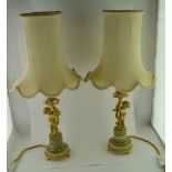A PAIR OF TABLE LAMPS, cast gilt metal putti stems, on green onyx bases, with cream fabric shades,