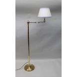 A BRASS READING LIGHT, floor standing with articulated arm, with cream fitted shade