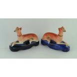 A PAIR OF 19TH CENTURY POTTERY INKWELLS, modelled as reclining long dogs, on cobalt blue bases,