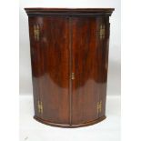 A 19TH CENTURY BOW FRONTED CORNER CUPBOARD, having two plain crossbanded doors, opening to reveal