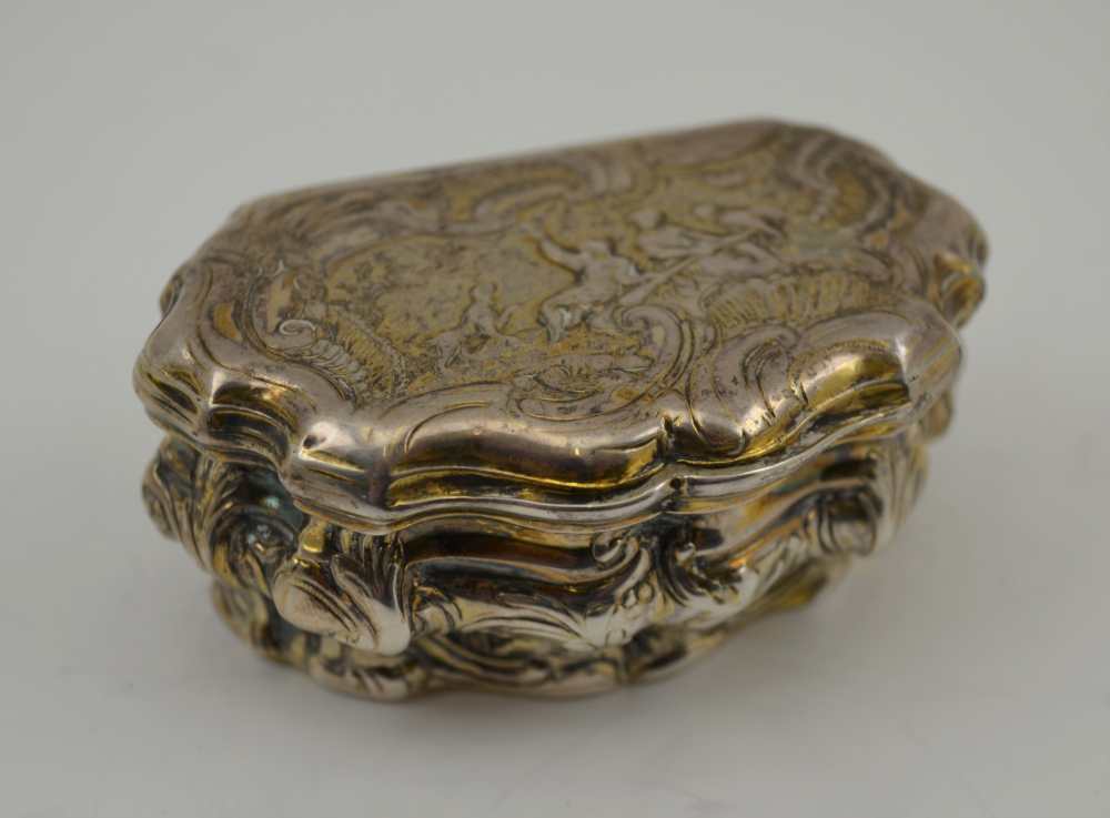 AN 18TH CENTURY PARCEL GILT WHITE METAL CONTINENTAL SNUFF BOX, of Rococo serpentine form, repousse