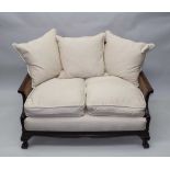AN EDWARDIAN TWO-SEATER SOFA, stained wood carved frame, with split cane panels, raised on paw feet,