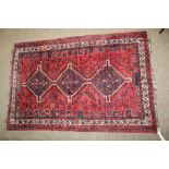 AN IRANIAN WOOL RUG, red ground, three central motifs, castellated and deeply bordered, fringed,