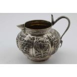 AN EASTERN WHITE METAL CREAM JUG, of lobed form, with repousse panel decoration, including elephant,