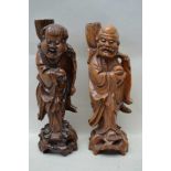 A PAIR OF CHINESE CARVED HARDWOOD IMMORTALS wearing robes, each carrying a large lotus blossom