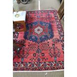 A WOVEN WOOLEN FLOOR RUG of red & blue stylised floral forms