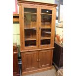 A MODERN PINE TWO PIECE BOOKCASE / DISPLAY UNIT, the upper section having twin glazed doors