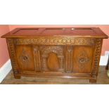 A 20TH CENTURY REPRODUCTION OAK COFFER with carved tri-panel front raised on stile supports, 120cm