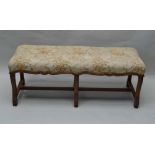 A WOODEN FRAMED THREE PERSON PAD TOP STOOL supported on six carved cabriole shaped legs, united by