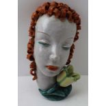 A "GOLDSHEIDER" AUSTRIAN POTTERY WALL MASK, the face with red curly hair and a flower at her chin,
