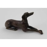 A 20TH CENTURY CAST BRONZE LONG DOG, lying with front legs extended and paws crossed, 10cm long