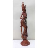 A 20TH CENTURY BALINESE CARVED WOOD GODDESS, in a sinuous dancing pose, wearing a crown, on lotus