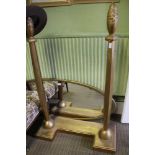 A LARGE GILT PAINTED OVAL PLAIN PLATE CHEVAL TYPE MIRROR on faceted column uprights and shaped