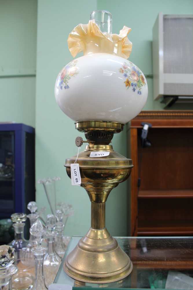 A BRASS BASED OIL LAMP with floral decorated globular shade