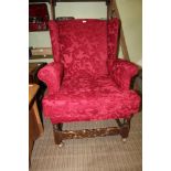 A BERGUNDY FLOCK EFFECT UPHOLSTERED WINGBACK ARMCHAIR