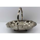 THOMAS LEVESLEY AN EDWARDIAN SILVER SWING HANDLED BASKET of embossed oval shaped form, on ball feet,
