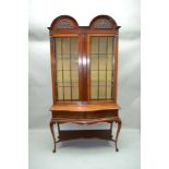AN EDWARDIAN MAHOGANY DISPLAY CABINET with twin arched pediment, over two plain bar glazed doors,