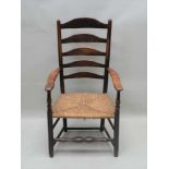 AN EARLY 19TH CENTURY VERNACULAR COUNTRY LADDER BACKED ARMCHAIR with rush seat, 107cm high