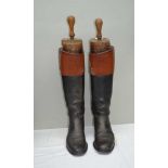 A PAIR OF TAN TOP BLACK HUNTING BOOTS with wooden trees