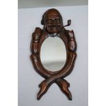 A LATE 19TH CENTURY EUROPEAN CARVED MIRROR FRAME, depicts a cross legged man with a glass and a pipe