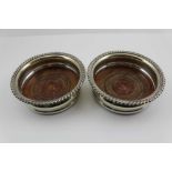 A PAIR OF VICTORIAN SILVER PLATED WINE BOTTLE COASTER with gadrooned rims and turned wood bases,