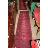 TWO WOVEN WOOL FLOOR RUNNERS, on a pigeon red ground, having central field of elephants feet,