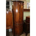 A WELL MADE REPRODUCTION MAHOGANY FREESTANDING CORNER CUPBOARD having carved cornice over bow