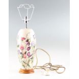 A Moorcroft table lamp with Sweet Pea pattern on white background, designed by Nicola Slaney, on oak