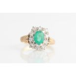 A 9ct yellow gold emerald and diamond cluster ring, set with a central oval cut emerald, measuring