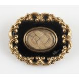 A Victorian enamel memorial brooch, featuring a glass fronted panel containing plaited hair,