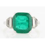 An Art Deco emerald and diamond ring, set with a central cushion cut emerald, measuring approx.