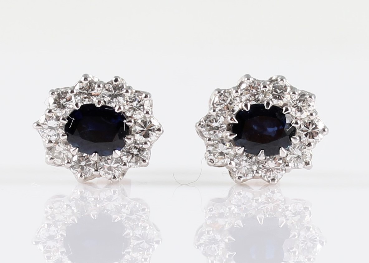 A pair of sapphire and diamond cluster stud earrings, each set with an oval cut sapphire,