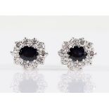 A pair of sapphire and diamond cluster stud earrings, each set with an oval cut sapphire,
