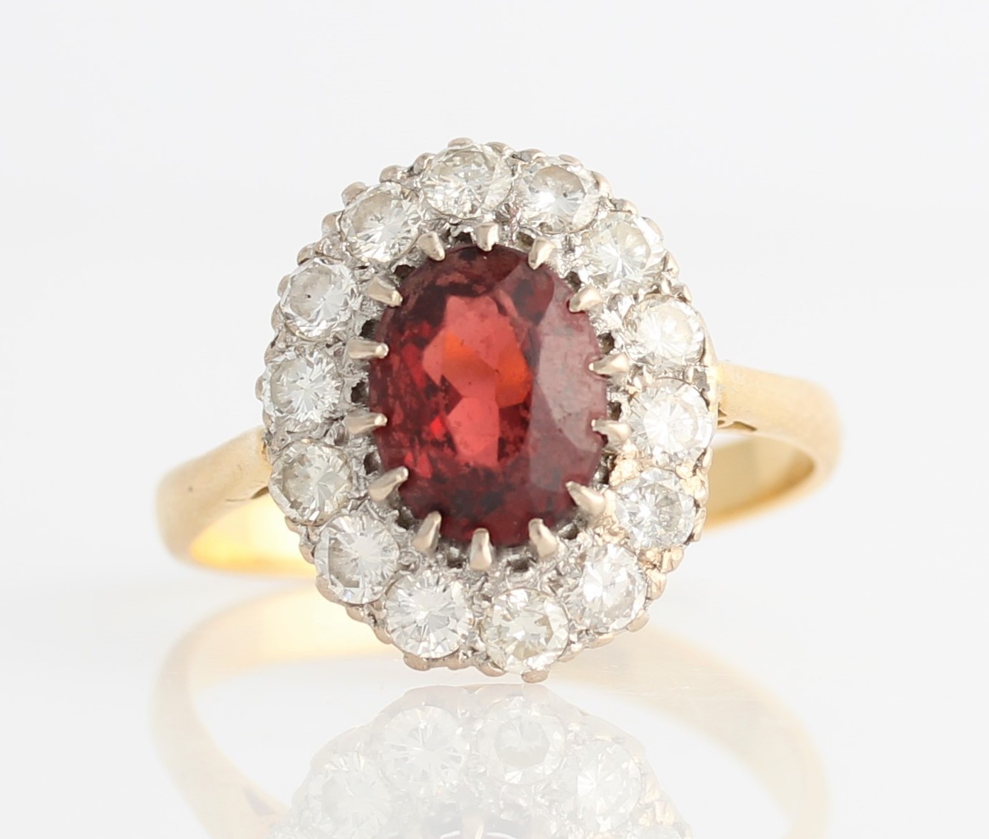 A garnet and diamond cluster ring, set with central oval cut garnet, measuring approx. 7x9mm,