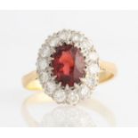 A garnet and diamond cluster ring, set with central oval cut garnet, measuring approx. 7x9mm,