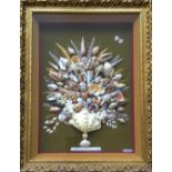 A framed shell art collage including seashells, coral and painted leaves on green background,