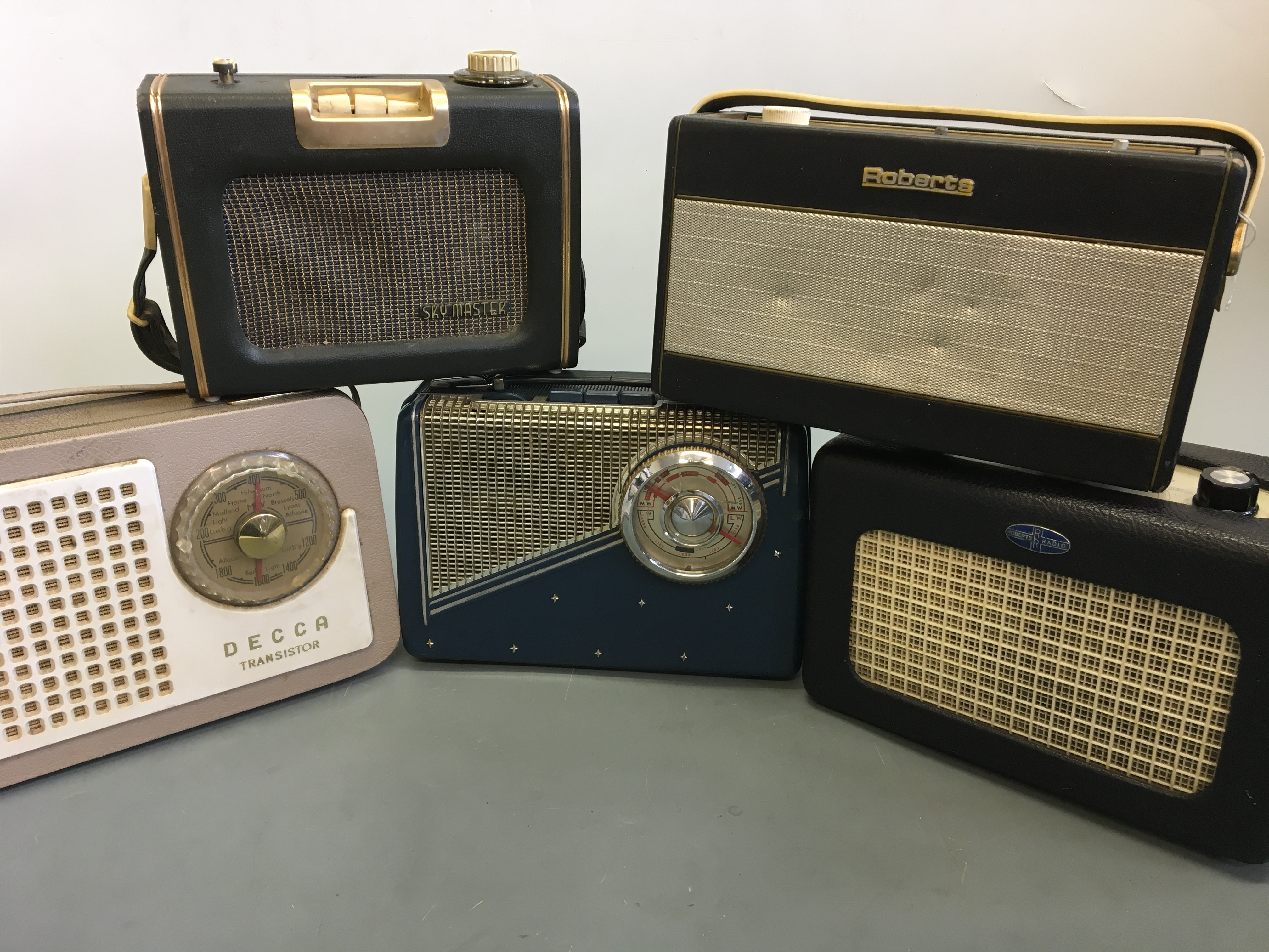 Five radios including blue KB Transistor, two black Roberts, Skymaster and beige Decca Transistor.