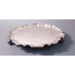 A hallmarked silver tray with scroll shell design pie crust edge on three feet, inscription in